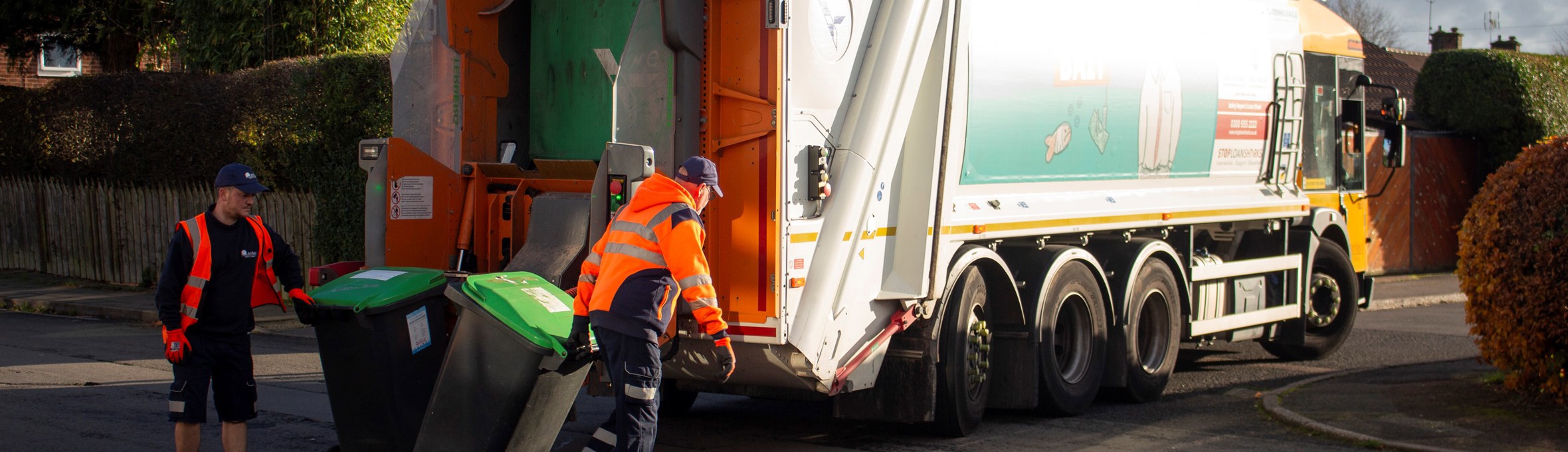 2 refuse workers behind a bin lorry